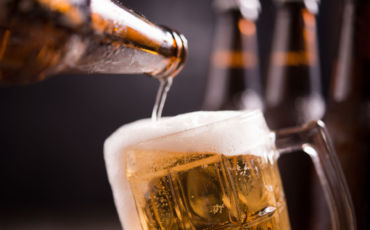 Glass bottles of beer with glass and ice on dark background